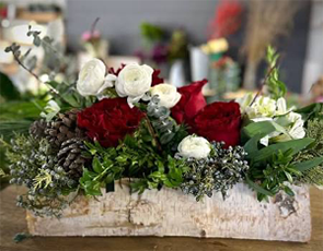 Red and white flowers, festive greens, pine cones and hints of silver floating in a birch loge